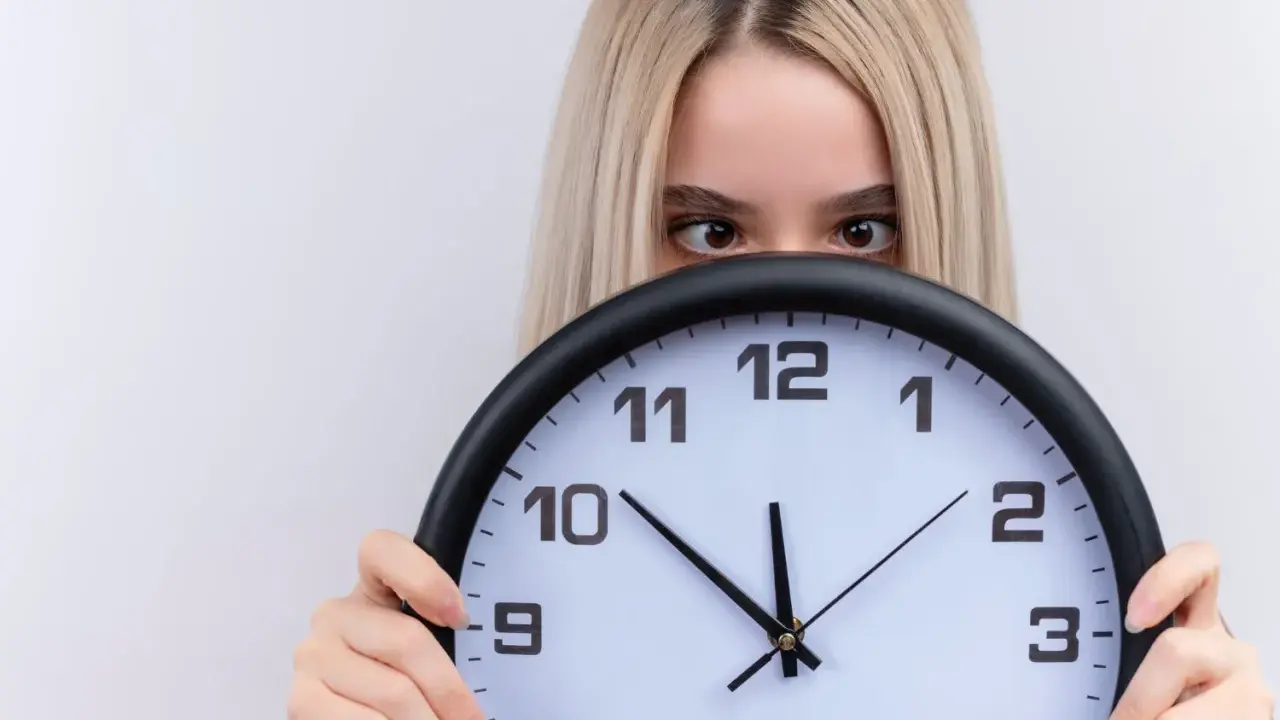 Dziewczyna z blond włosami ukrywa się za zegarem, patrząc zza niego. Czyżby czas miał dla niej jakieś szczególne 2233 znaczenie?