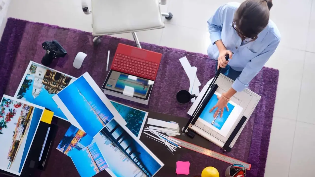 Kobieta przycina wydruki wykonane techniką druk lateksowy. Na stole leżą zdjęcia, laptop i aparat.