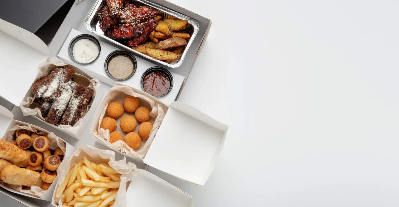 Variedad de comida para llevar: alitas, costillas, papas fritas, croquetas y pan. ¡Todo listo para disfrutar!