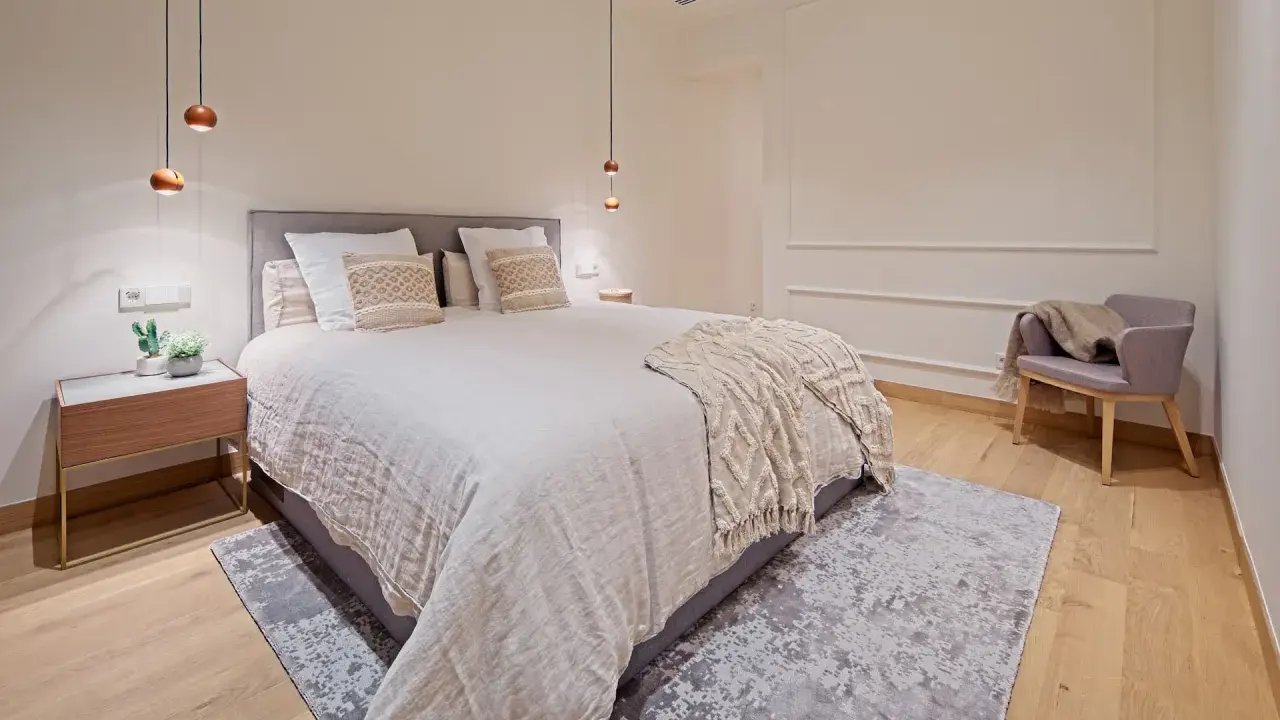 Dormitorios relajantes con cama amplia, manta texturizada, sillón acogedor y luces colgantes.