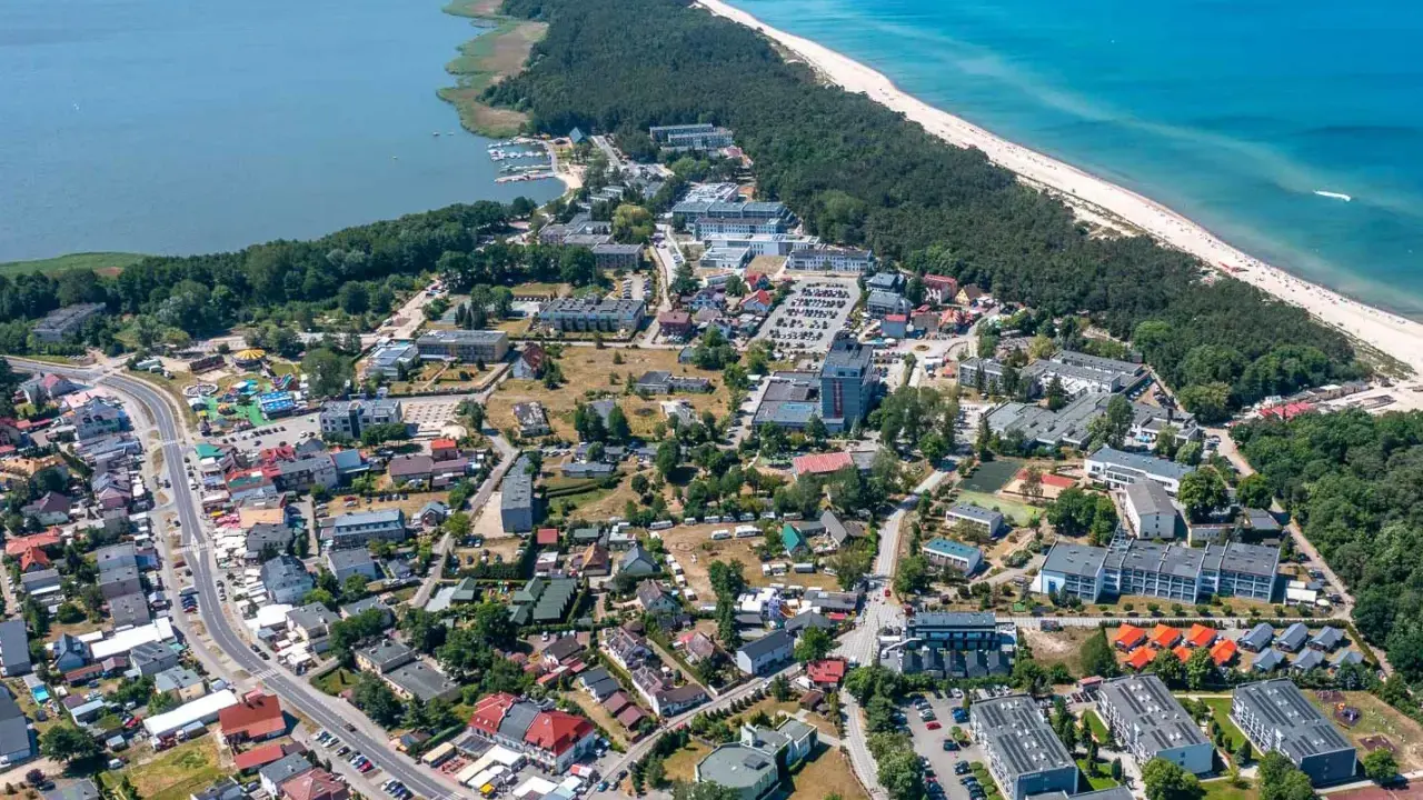 Dąbki atrakcje: widok z lotu ptaka na nadmorską miejscowość z jeziorem, plażą, lasem i zabudowaniami.