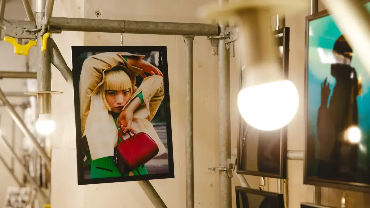 Plakat z kobietą w beżowym płaszczu i zielonym swetrze, trzymającą czerwoną torebkę. Stylizacja przypomina modę z **Pezet Tokyo**.
