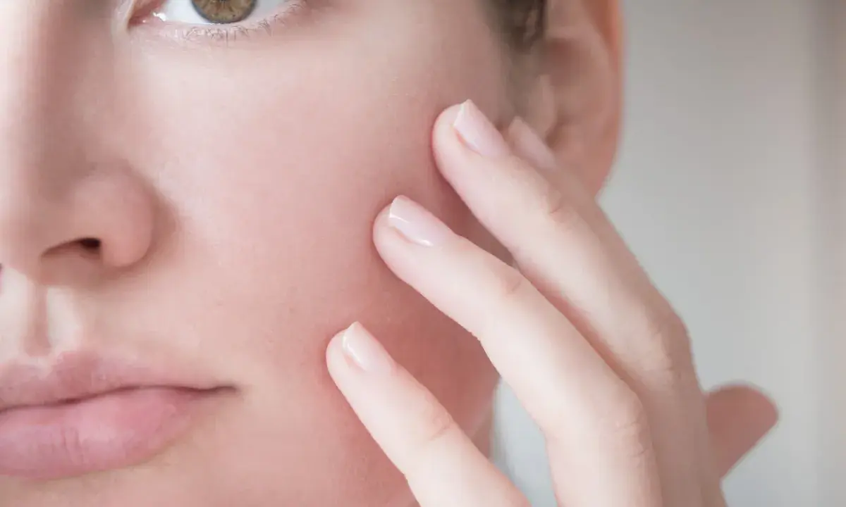 Dita accarezzano delicatamente il viso, mostrando una pelle reattiva e sensibile, bisognosa di cure delicate.