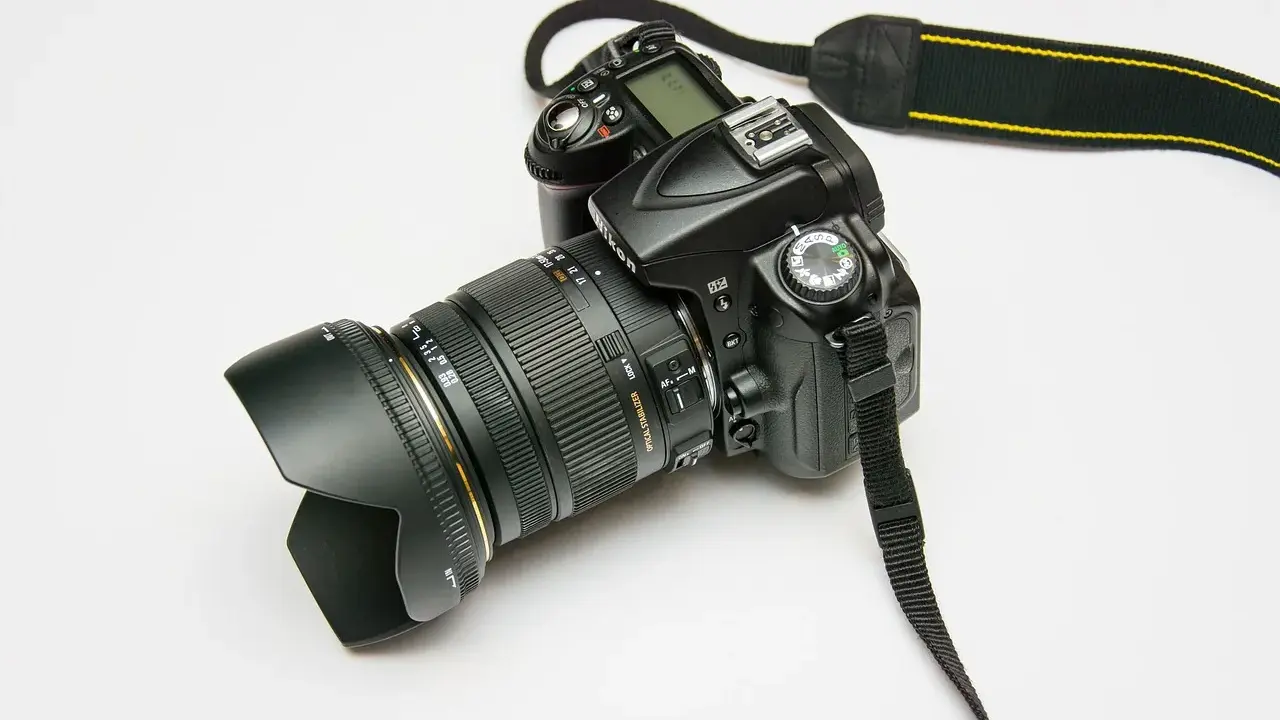 Czarny aparat fotograficzny z obiektywem i paskiem na białym tle.