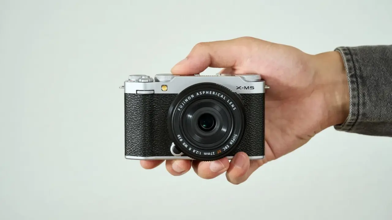 Mano sujetando una cámara Fujifilm X-M5 plateada y negra, lista para capturar momentos.