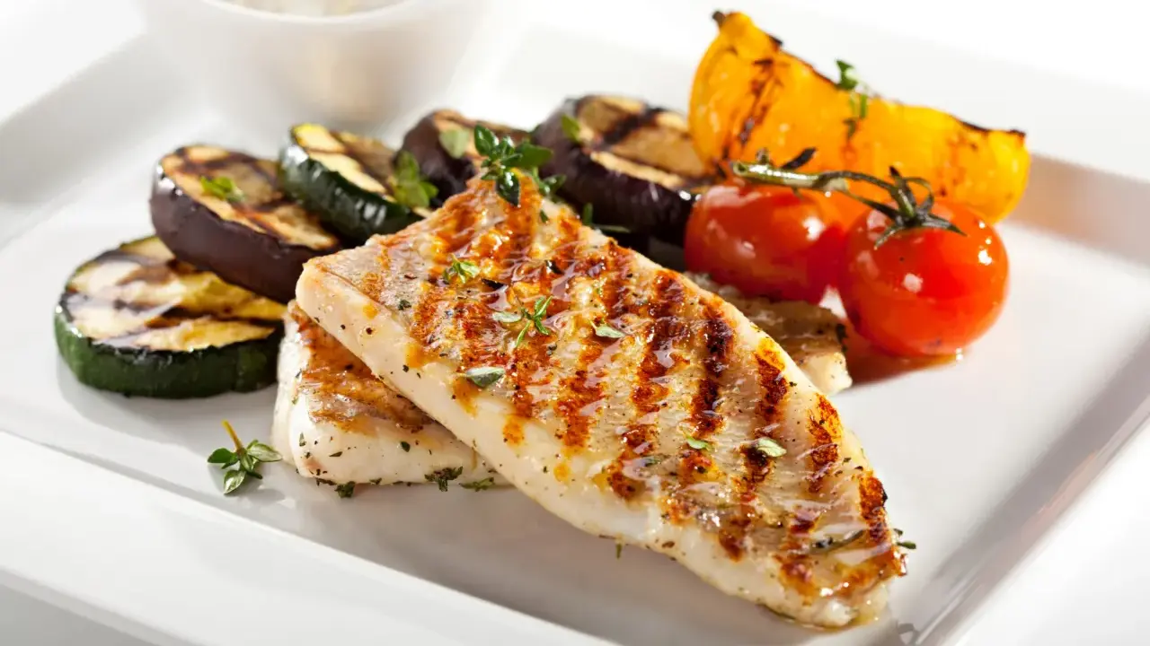 Gebratener Seelachs mit gegrilltem Gemüse wie Zucchini, Aubergine und Tomaten, garniert mit Kräutern.