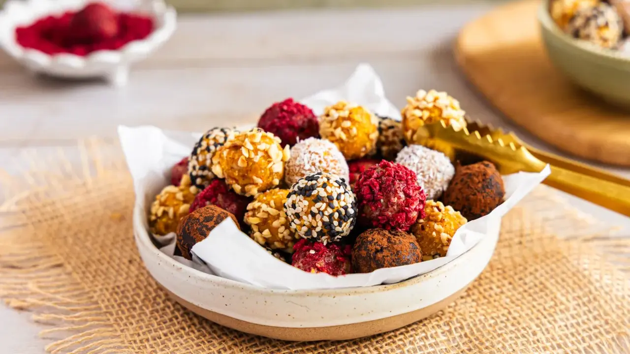 Schüssel voller bunter Energy Balls, perfekt für ein schnelles energy balls rezept. Mit Nüssen, Kokos, Kakao und Beeren verfeinert.