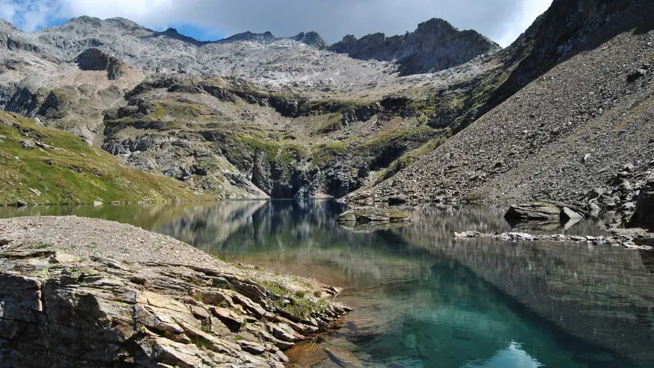 Riflessi perfetti sul lago nero, incastonato tra montagne rocciose e verdi pendii.