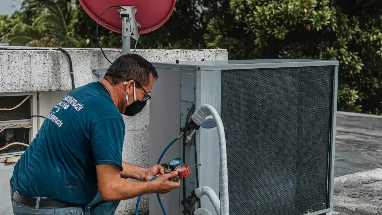 Technik w masce przeprowadza wymianę czujnika ciśnienia klimatyzacji na dachu, używając manometrów.
