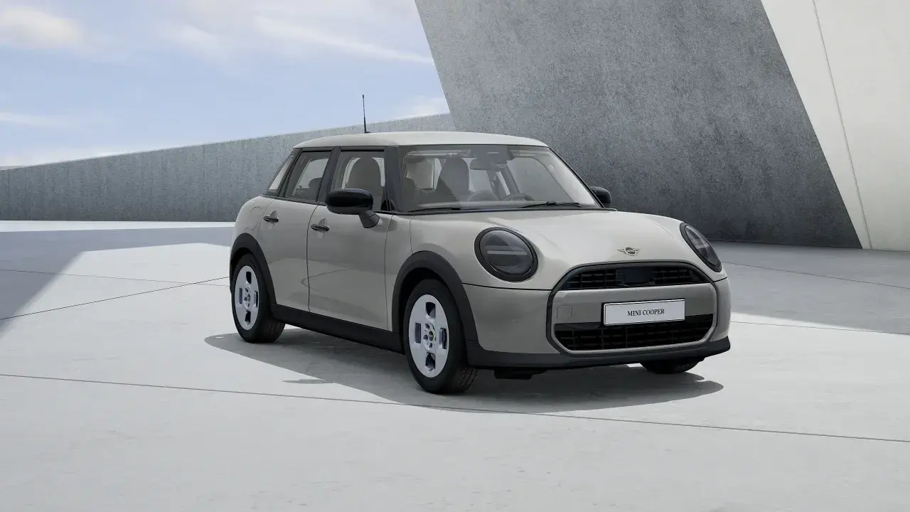 Mini Cooper 5 puertas en color gris claro, con llantas plateadas, estacionado en una zona de concreto con arquitectura moderna.