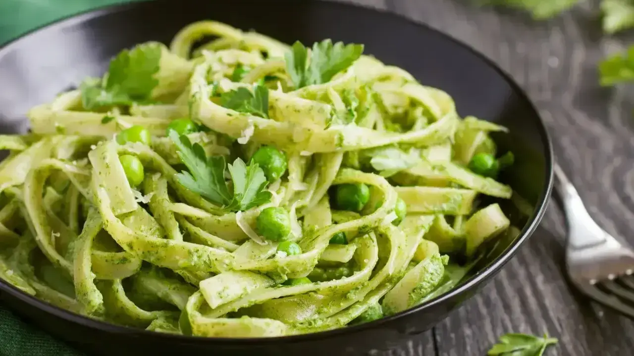 Pyszne tagliatelle z zielonym pesto, groszkiem i listkami pietruszki w czarnej misce.