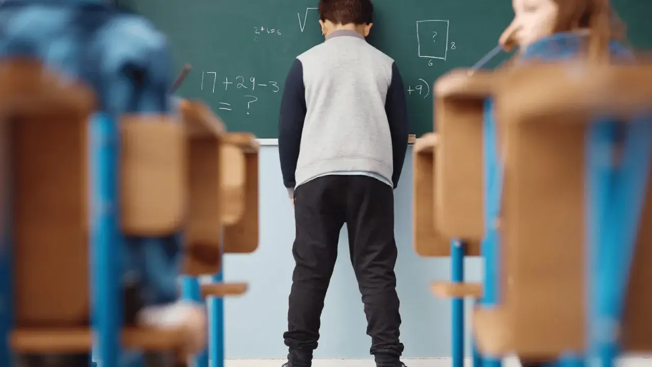 Chłopiec stoi przed tablicą z zadaniami matematycznymi.
