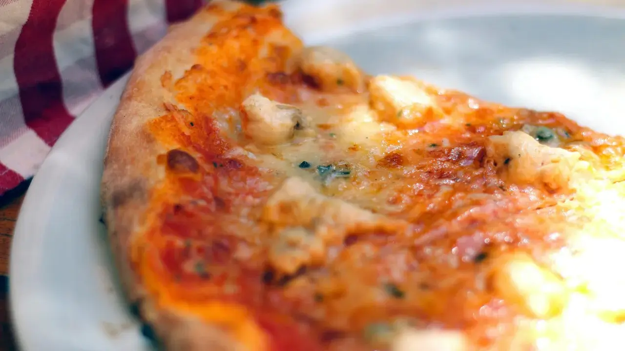 Tranche de pizza appétissante sur une assiette blanche, avec une serviette à carreaux rouges et blancs. Une recette parfaite avec de la farine sans gluten pour pizza.