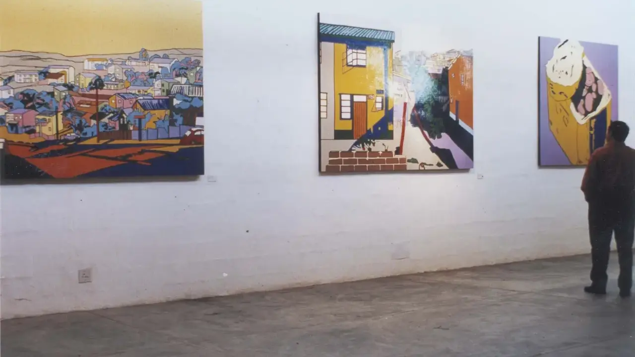 A person contemplates vibrant, stylized paintings in an art gallery, each piece curating meaning through bold colors and urban landscapes.