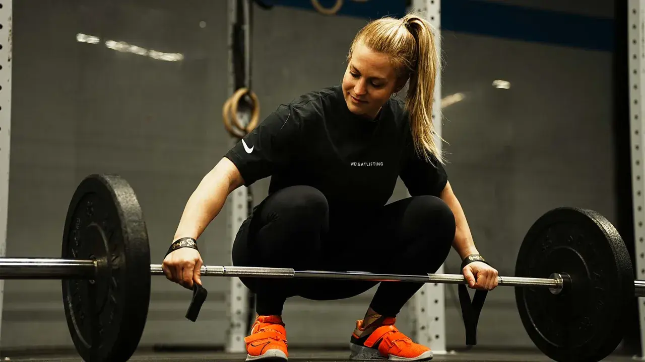 Eine Frau in Sportkleidung bereitet sich auf das Gewichtheben vor. Eine **1 Woche Trainingspause sinnvoll** für Regeneration und neue Kraft.