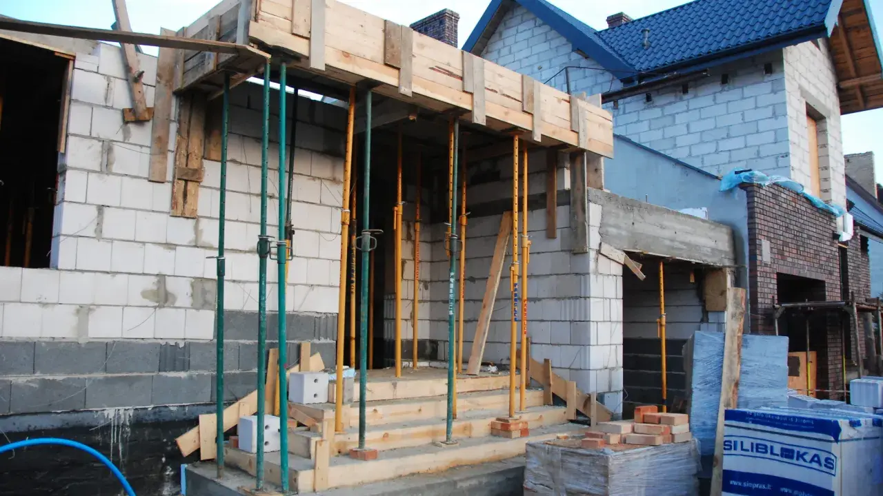 Budowa domu w toku. Drewniana konstrukcja stropu podtrzymywana przez liczne metalowe podpory.