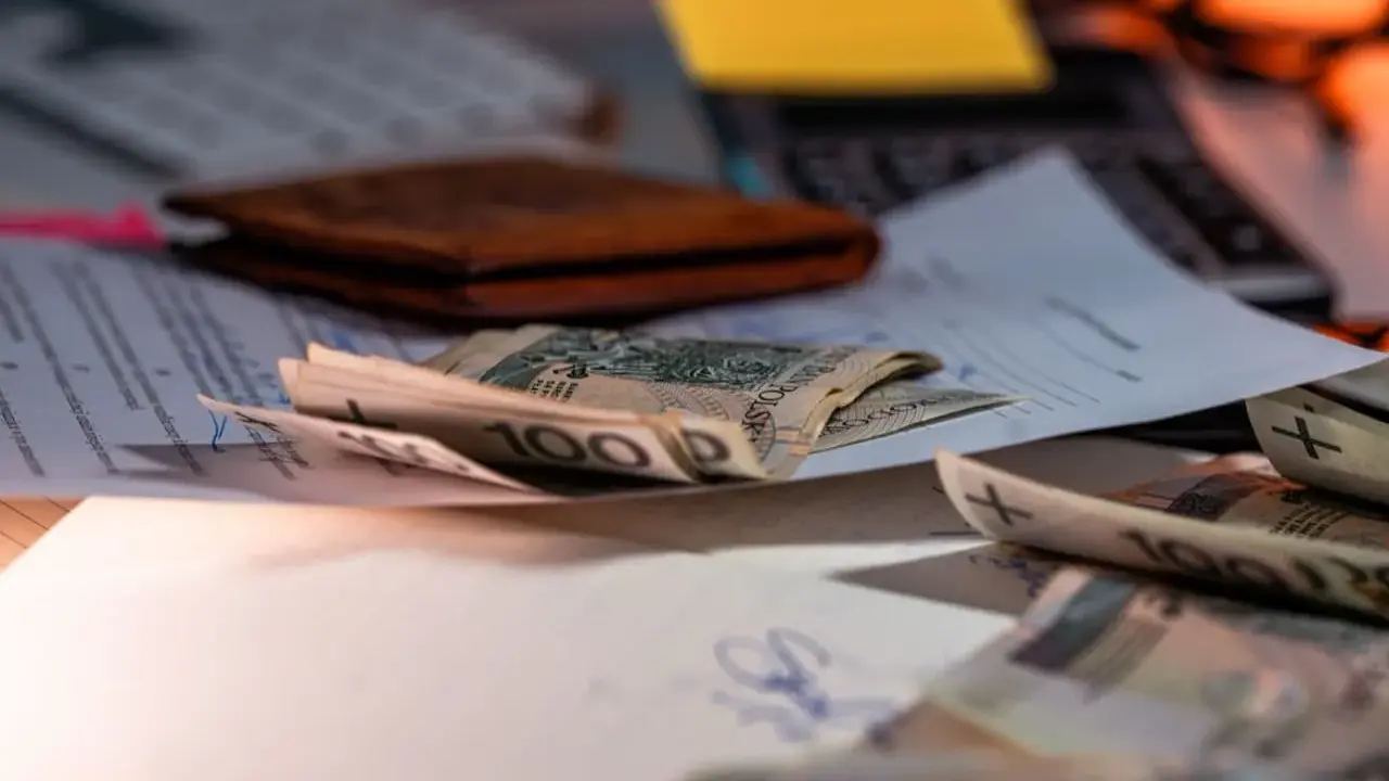Pieniądze na dokumentach, portfel i klawiatura. Symbolizują wsparcie finansowe, np. refundację pieluchomajtek dla osób ze znacznym stopniem niepełnosprawności.