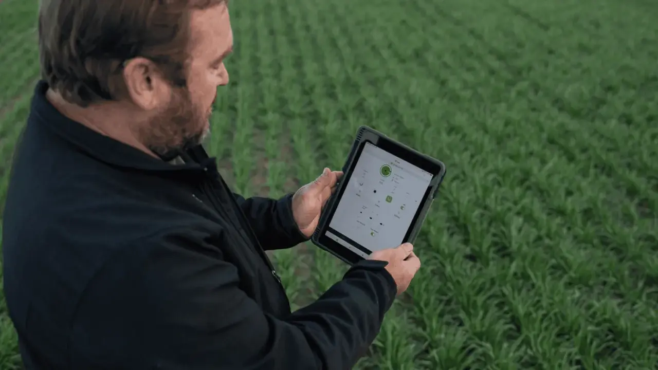Farmer uses a tablet to monitor crop health and optimize yields, showcasing the power of digital farming in a lush green field.