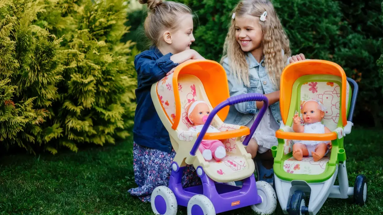 Dwie dziewczynki bawią się lalkami w wózkach, odgrywając różne etapy życia dziecka.