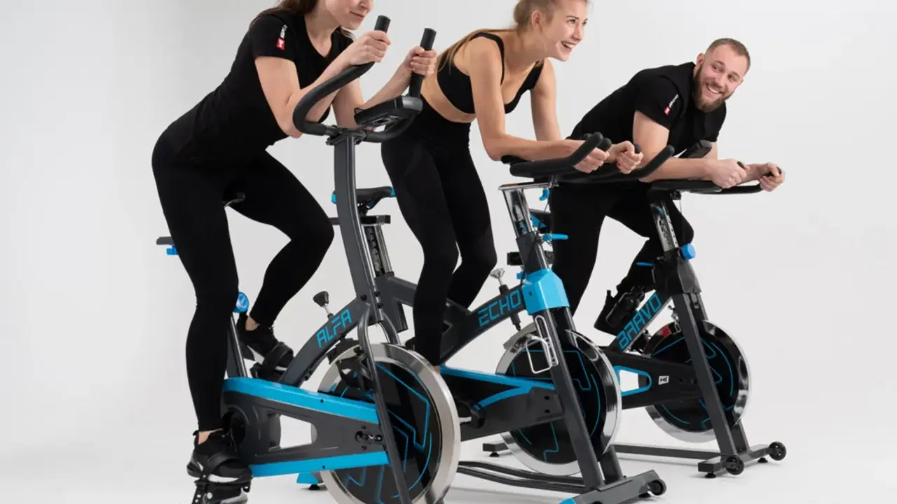Trzy osoby ćwiczą na rowerach stacjonarnych. To świetny trening spinningowy!