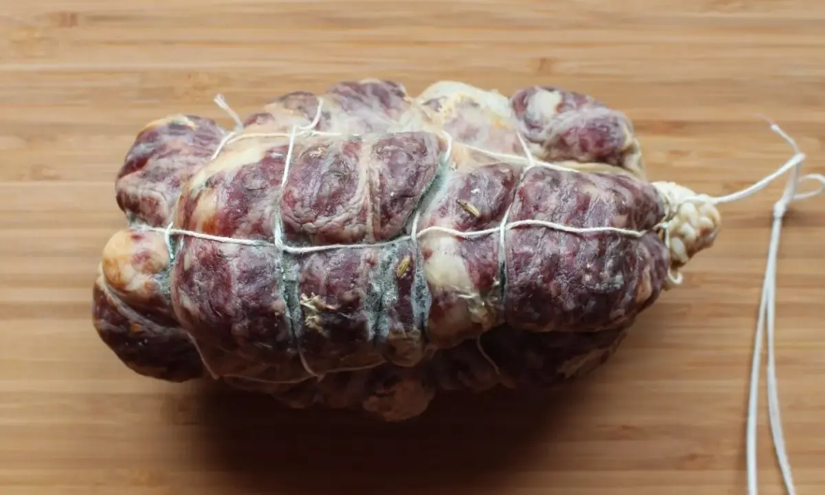 Spianata, włoska kiełbasa wieprzowa, związana sznurkiem, leży na drewnianej desce.