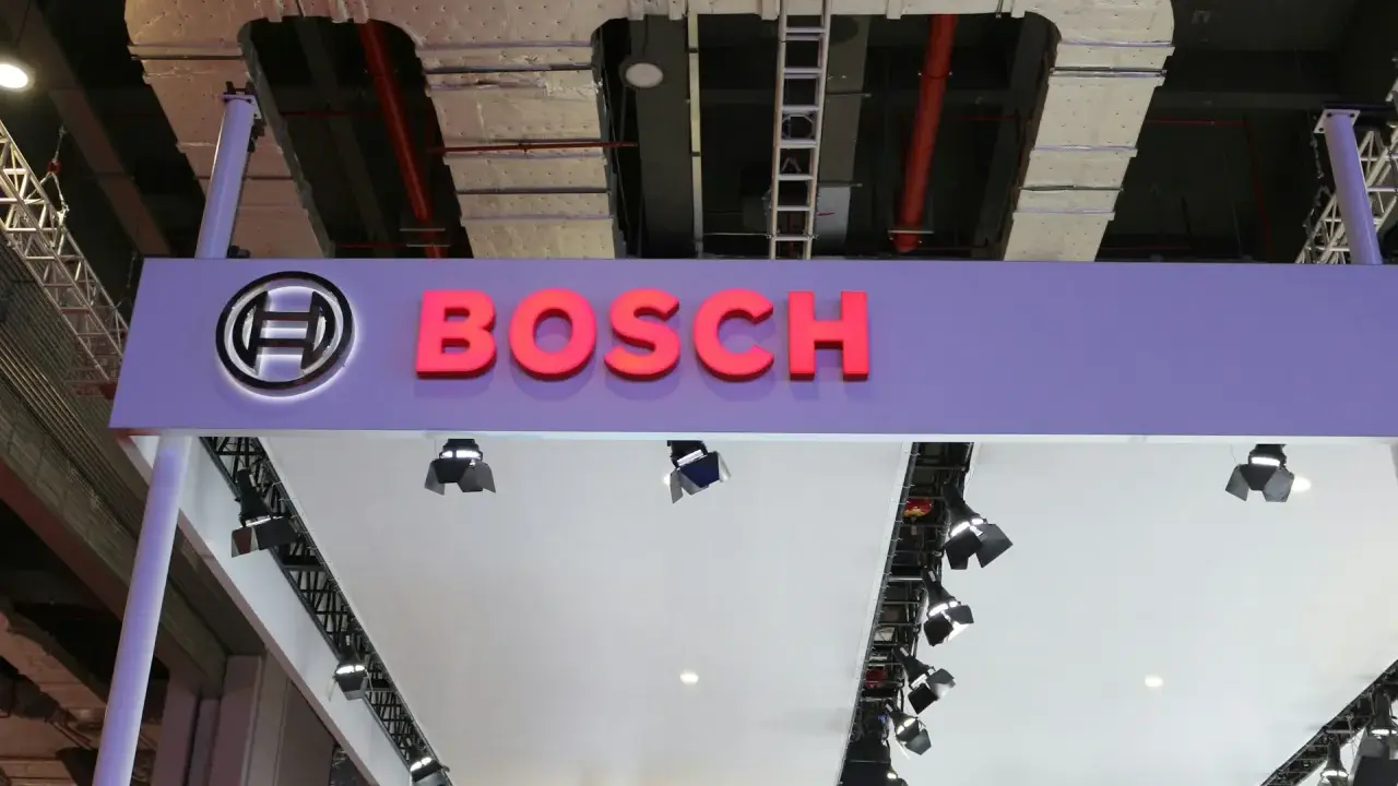 Logo Bosch i nazwa firmy na fioletowym tle. W tle widać instalacje przemysłowe, przewody i drabiny, sugerujące miejsce, gdzie odbywa się produkcja.