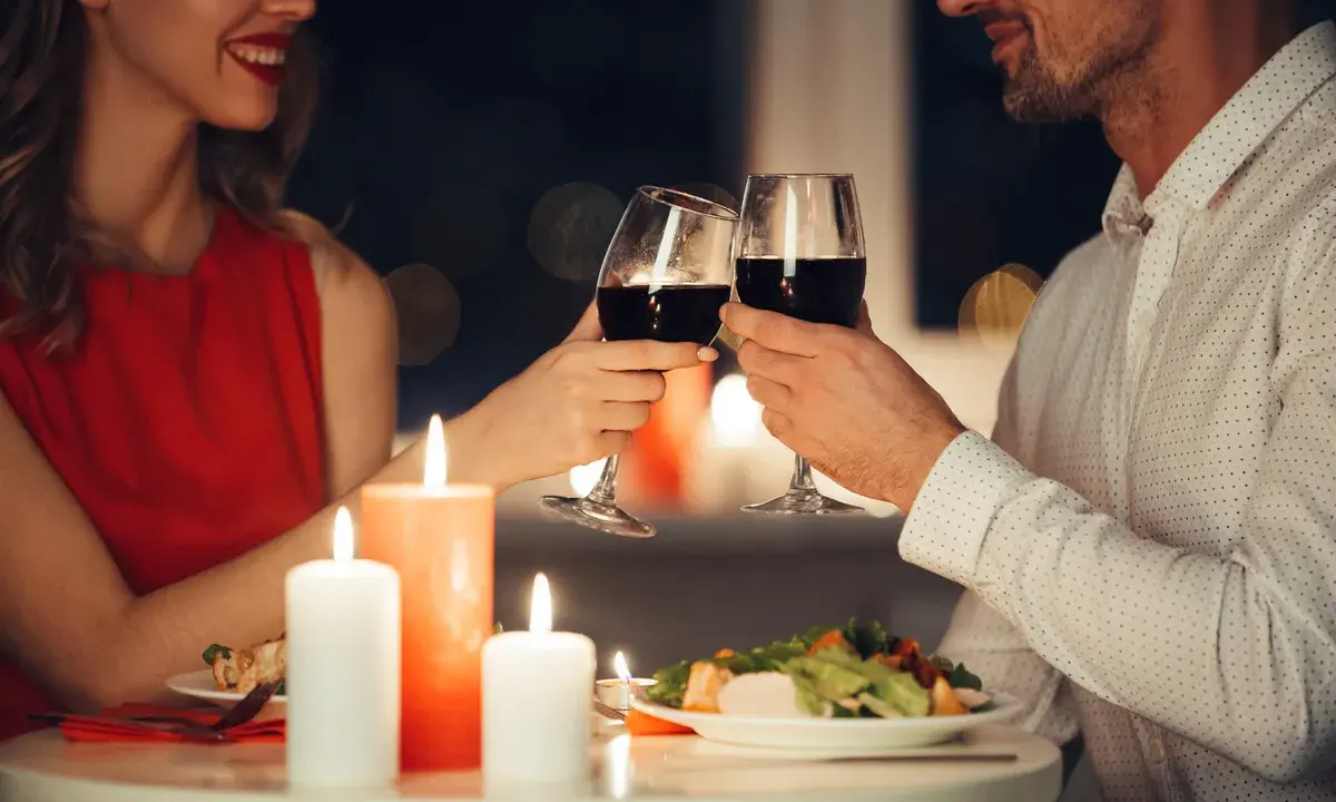 Romantyczna kolacja przy świecach. Para wznosi toast kieliszkami czerwonego wina, uśmiechając się do siebie.