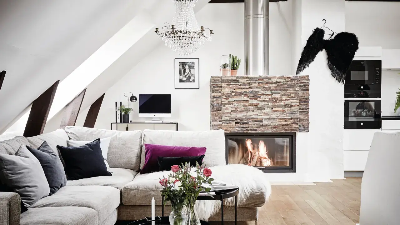 Mysigt vardagsrum med öppen spis, soffa och ett soffbord i 3 delar med blommor och ljus.