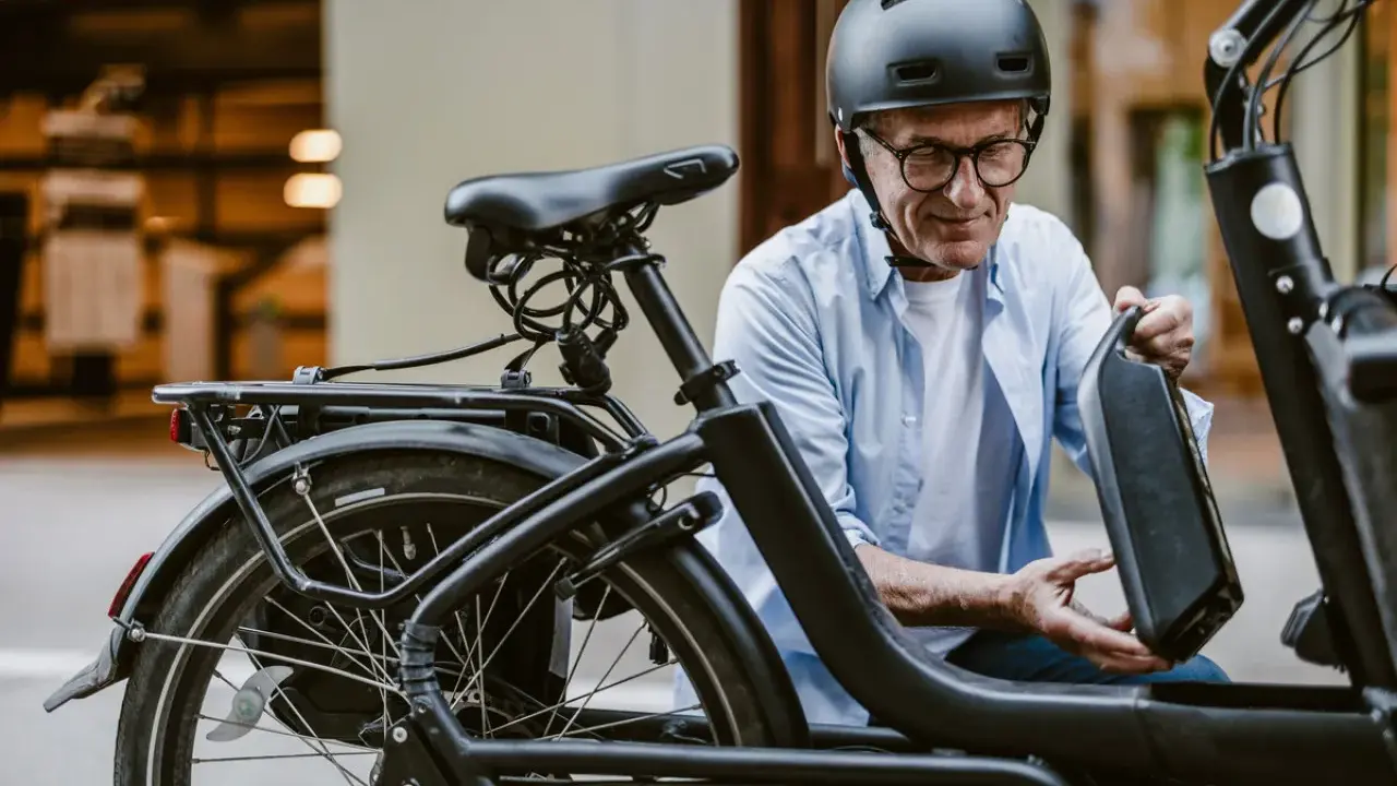 Un homme en casque retire la batterie de son vélo électrique, prêt pour l'immatriculation vélo électrique.