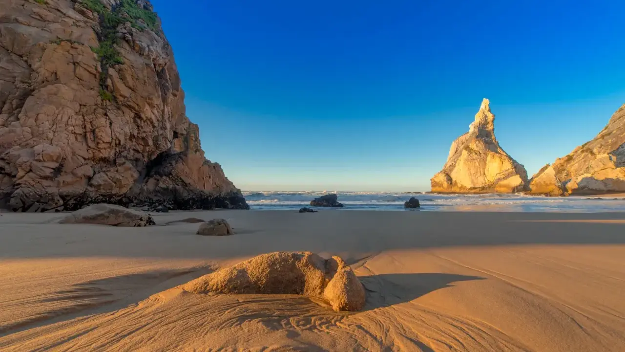 Goldene Sanddünen und Felsen am Praia da Ursa im warmen Abendlicht.