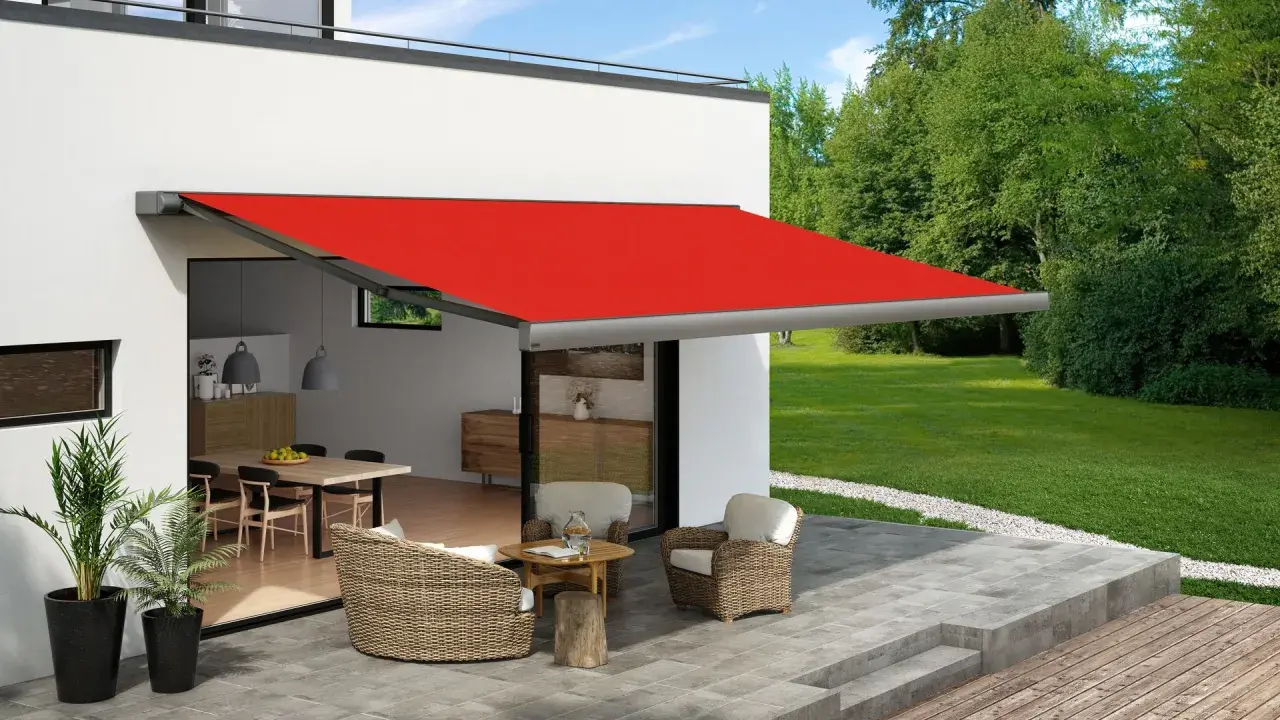 Toldo rojo extendido sobre un patio con muebles de mimbre, ofreciendo ideas para dar sombra en un patio.