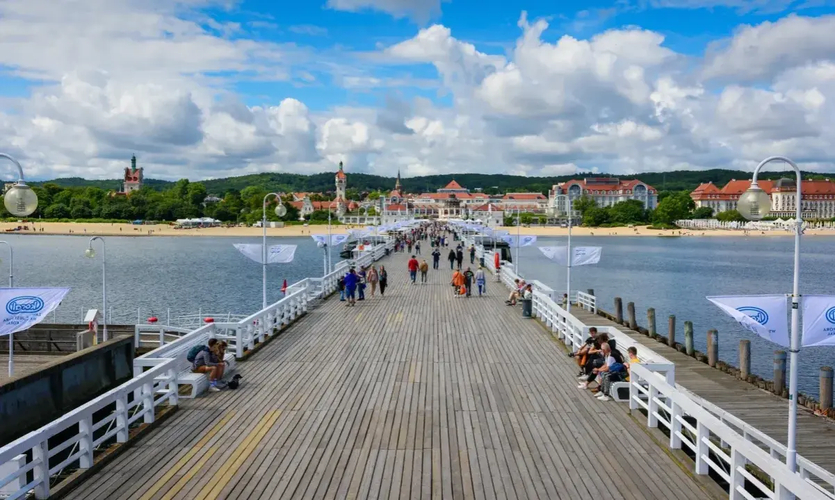Spacer w Sopocie tętni życiem. Ludzie spacerują po drewnianym molo, podziwiając widok na plażę i zabytkowe budynki.
