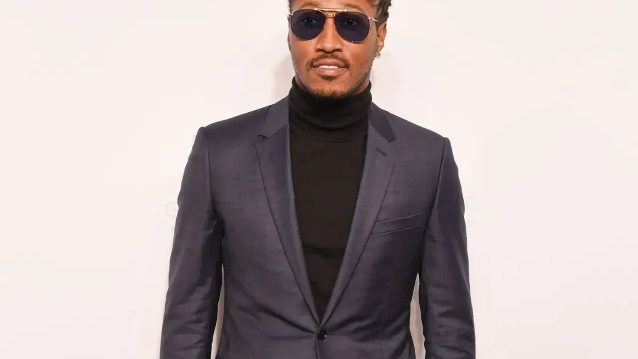 A man in a sharp black suit with a turtleneck, sporting stylish sunglasses.