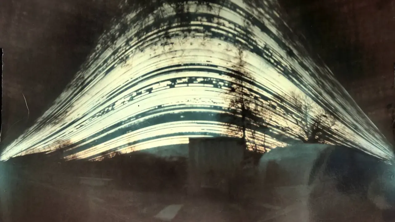 Paesaggio distorto con alberi e strutture, catturato con un **foro stenopeico**. Le strisce luminose suggeriscono un lungo tempo di esposizione.