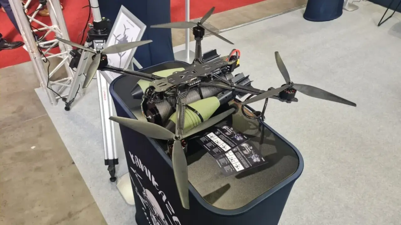 Ich sehe einen großen, schwarzen Quadrocopter mit grünen Zylindern, der auf einem Tisch steht. Die Propeller sind aus Carbon.