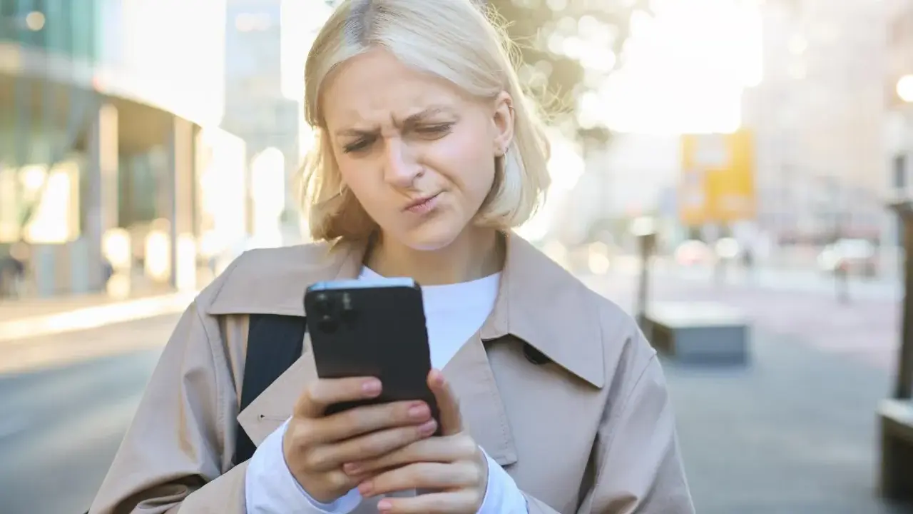 Zmarszczona kobieta patrzy na telefon, zastanawiając się, jak przestać zazdrościć innym.