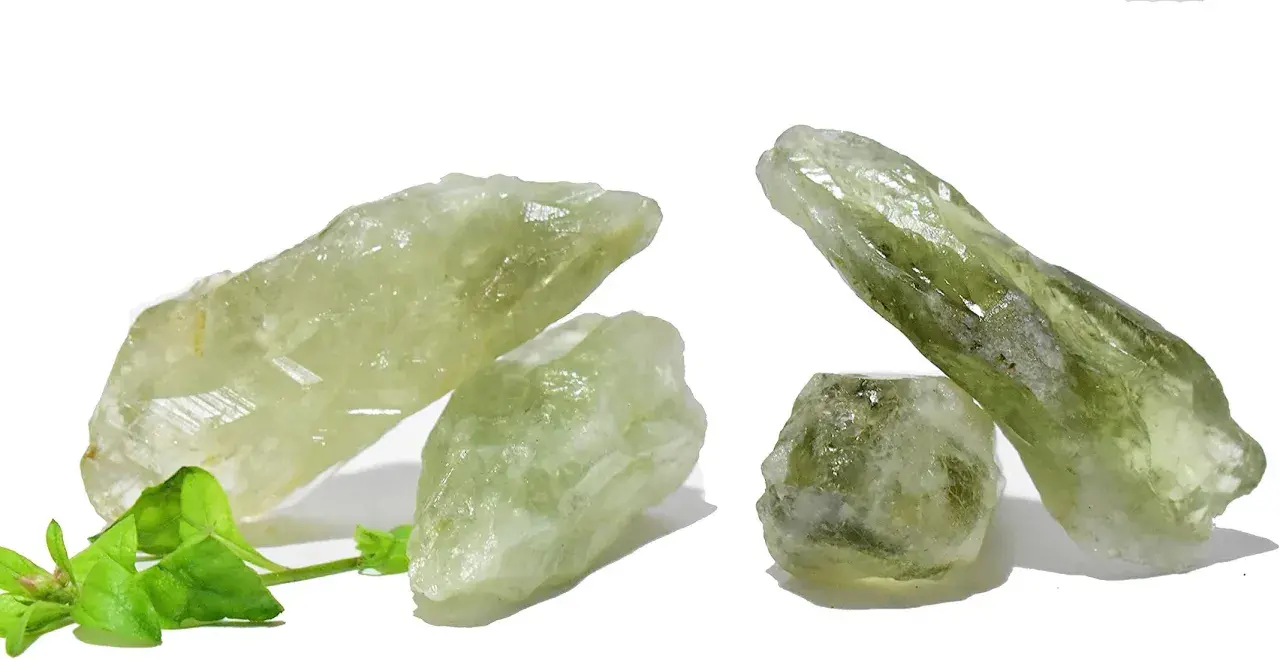 Cristalli grezzi di ametista verde, noti per il loro significato di crescita e rinnovamento, su sfondo bianco con foglie verdi.