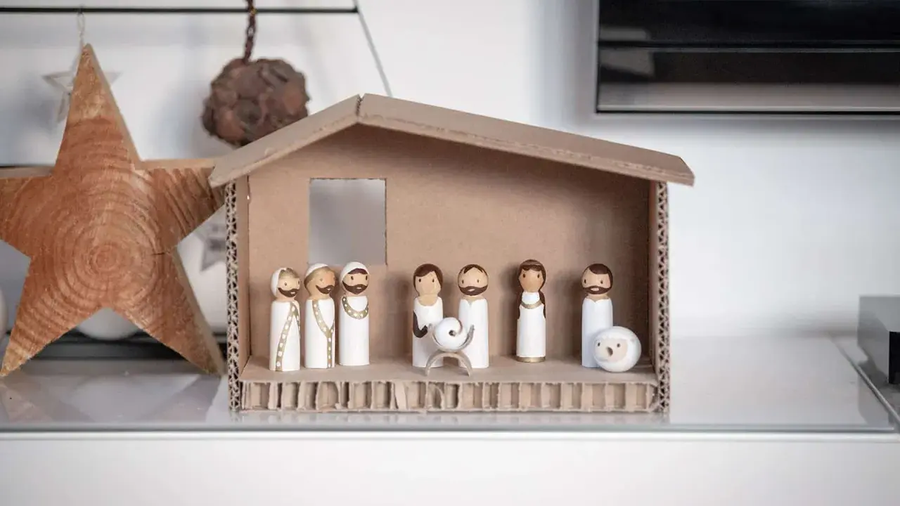 Eine einfache Krippe basteln Kinder mit Holzfiguren und Karton. Maria, Josef und das Jesuskind sind in der Mitte, umgeben von Hirten und einem Schaf.