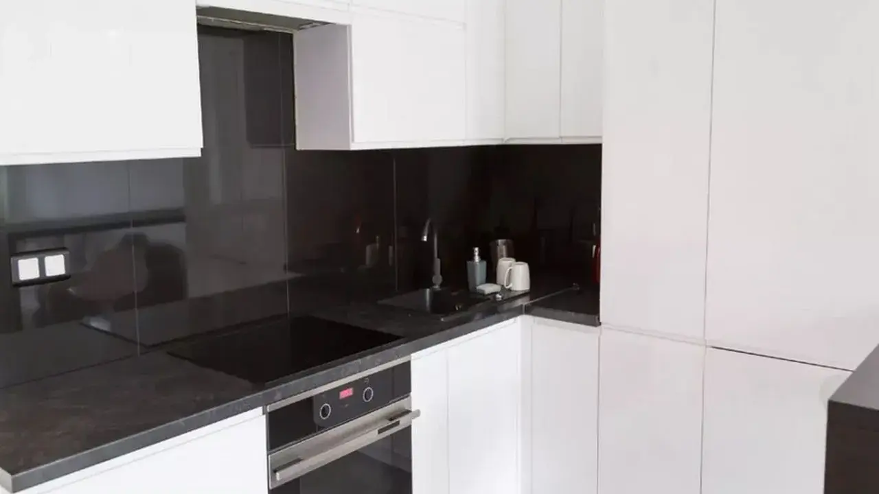 Nowoczesna, biała kuchnia z eleganckim, ciemnym blatem. Czarna płyta indukcyjna i zlew tworzą spójną całość.