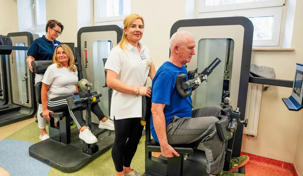 Rehabilitacja w Busko Zdrój: pan ćwiczy na siłowni pod okiem fizjoterapeutki, a pani z pomocą drugiej terapeutki. Sprawdź nasze sanatoria Busko Zdrój promocje!