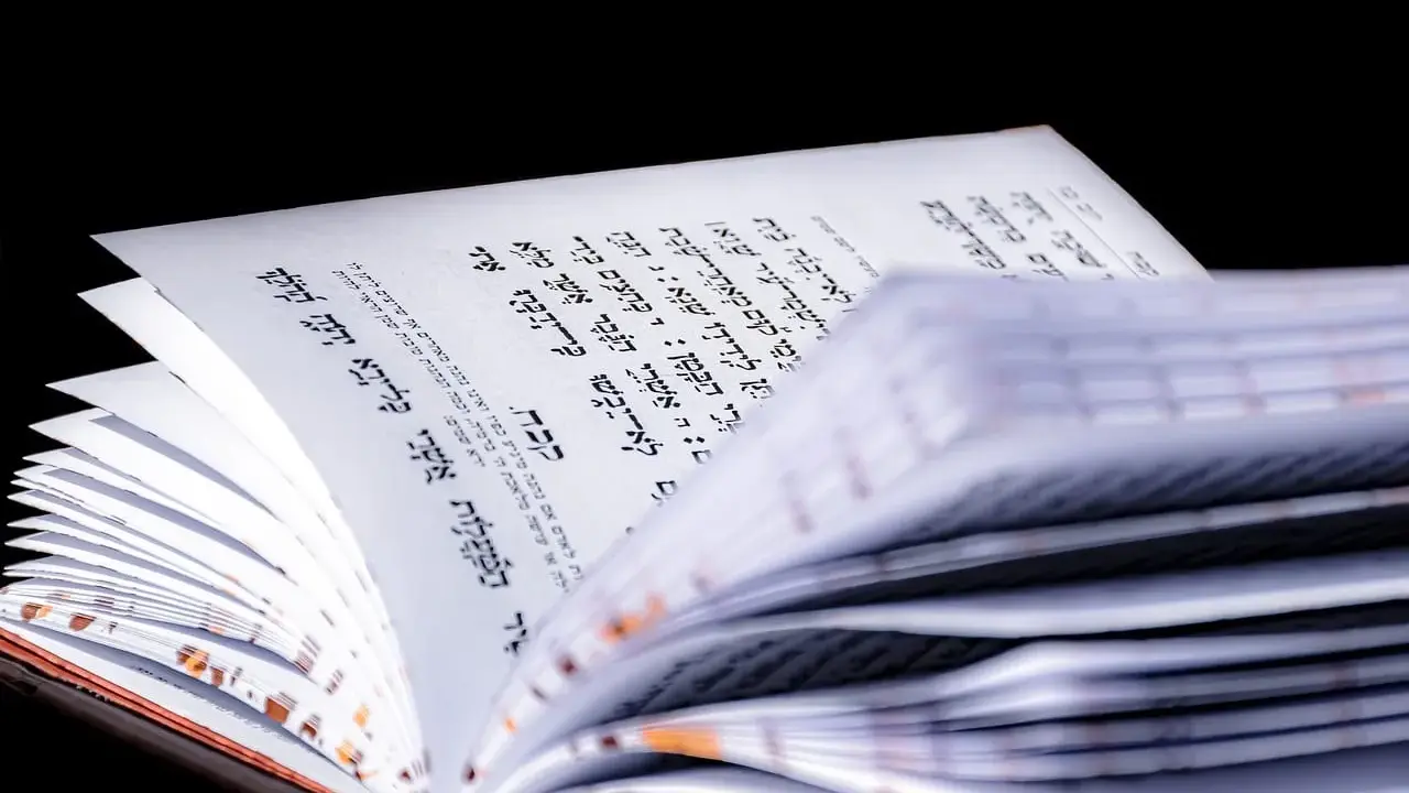 Otwarta księga z hebrajskim tekstem, fragment Psalmu 68. Strony są białe, tekst czarny, na czarnym tle.