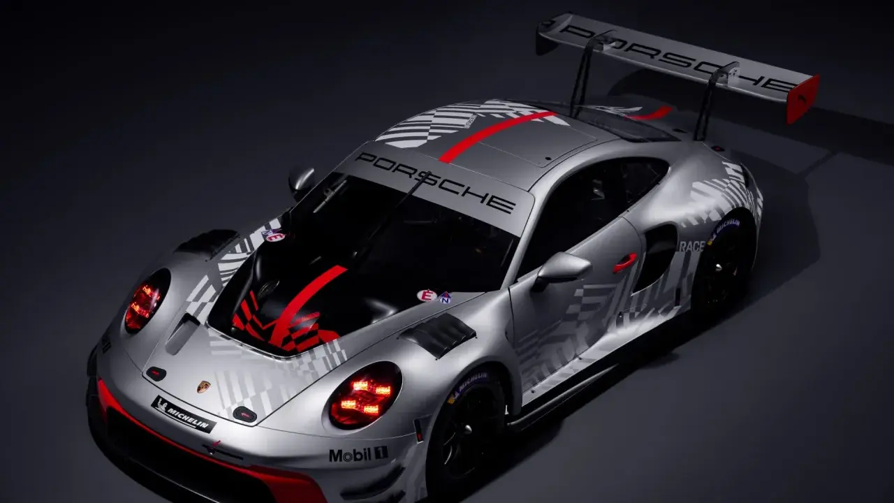 Silberner Porsche 911 GT3 R mit auffälligem Schachbrettmuster und roten Akzenten, bereit für die Rennstrecke.