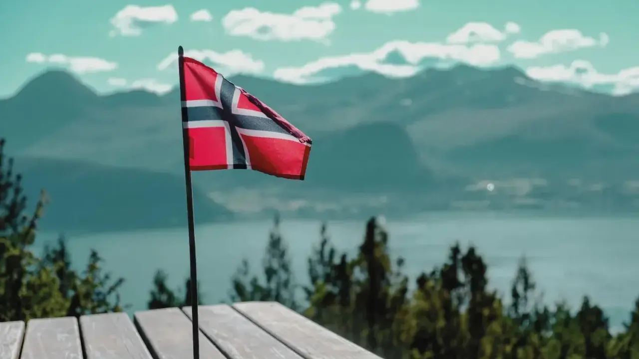 Norweska flaga na tle gór i jeziora. Pomyśl o tym, jak wysłać zwolnienie lekarskie do NAV, gdy jesteś w tak pięknych okolicznościach.
