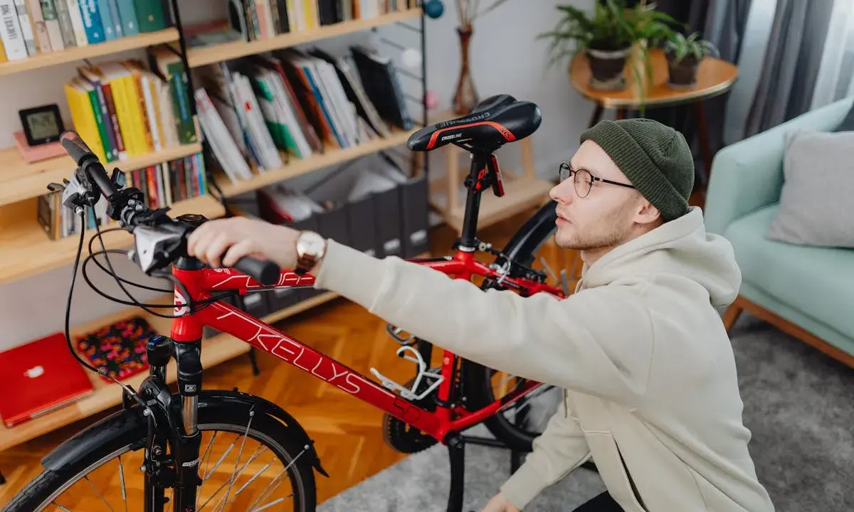 Mężczyzna przygotowuje rower do wysyłki w całości. W tle regał z książkami i rośliny.