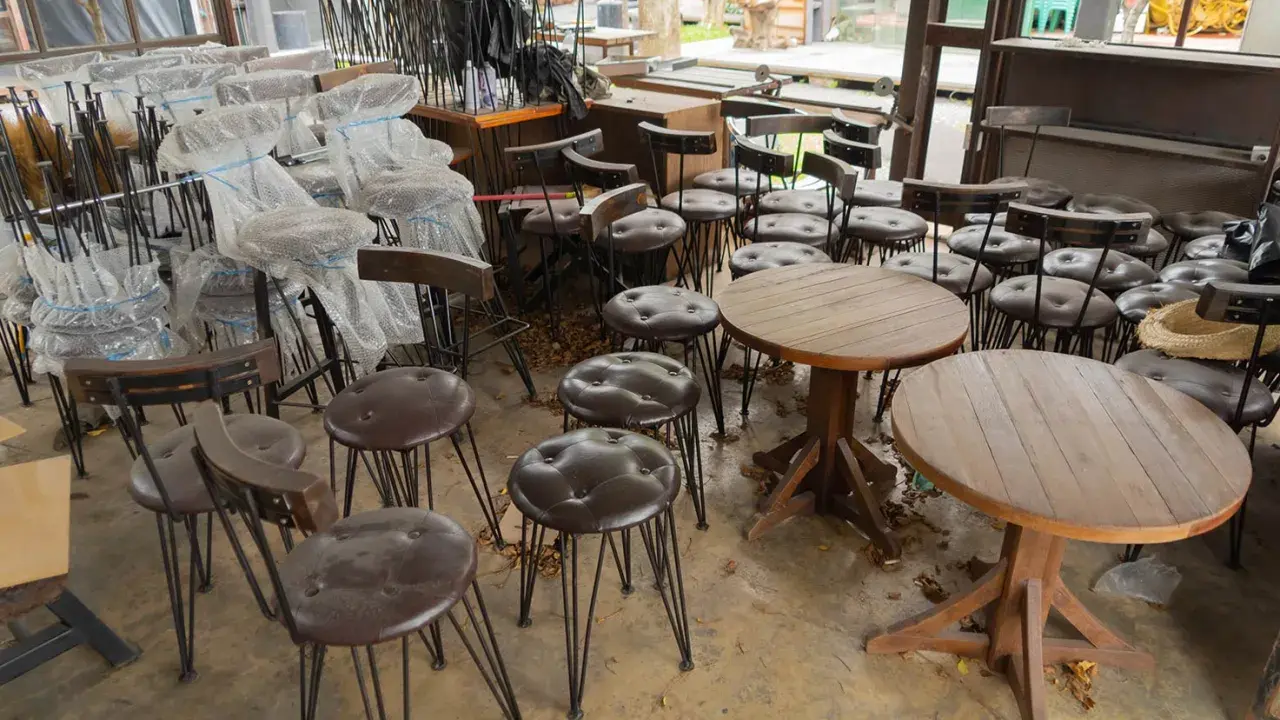 Viele gebrauchte Gastrostühle und runde Holztische stehen in einem Raum.