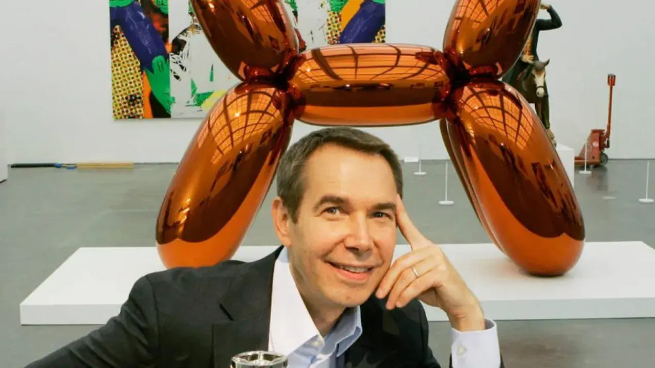 Jeff Koons posa junto a su icónica escultura perro globo naranja brillante en una galería de arte.