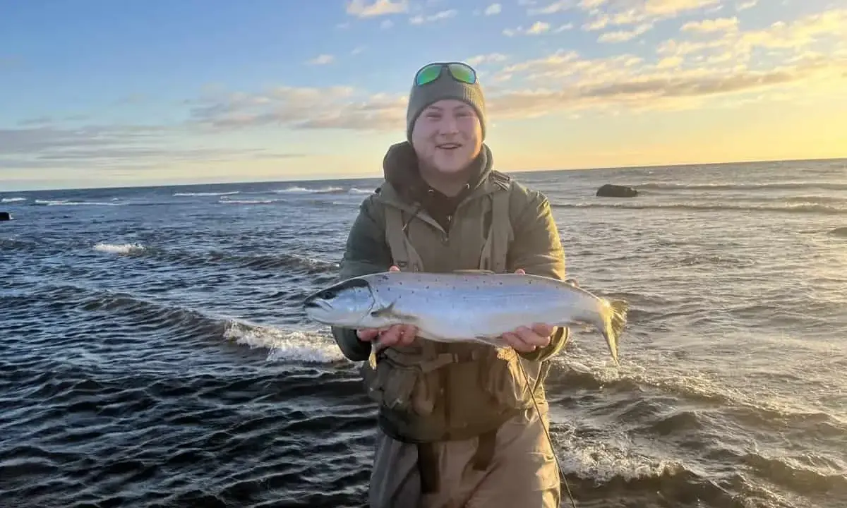 Glad fiskare med en fin öring vid havet, en lyckad dag med **trout fishing** i Sverige.