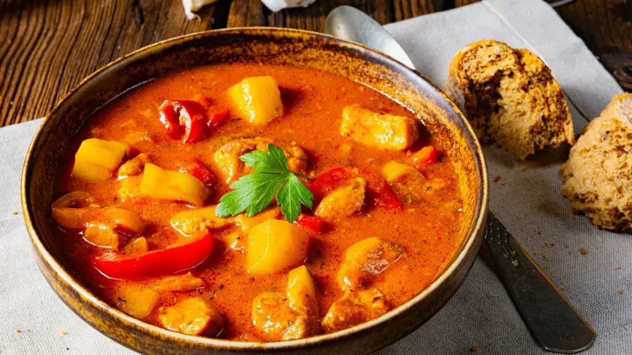 Aksamitna zupa gulaszowa, przepis babci, z kawałkami mięsa, ziemniaków i papryki, udekorowana natką pietruszki.