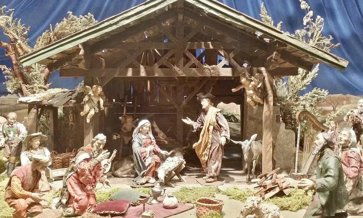 Krippenszene mit Maria, Josef und dem Jesuskind. Engel schweben über der Szene, die an Weihnachten im Mittelalter erinnert. Hirten und Musiker sind versammelt.