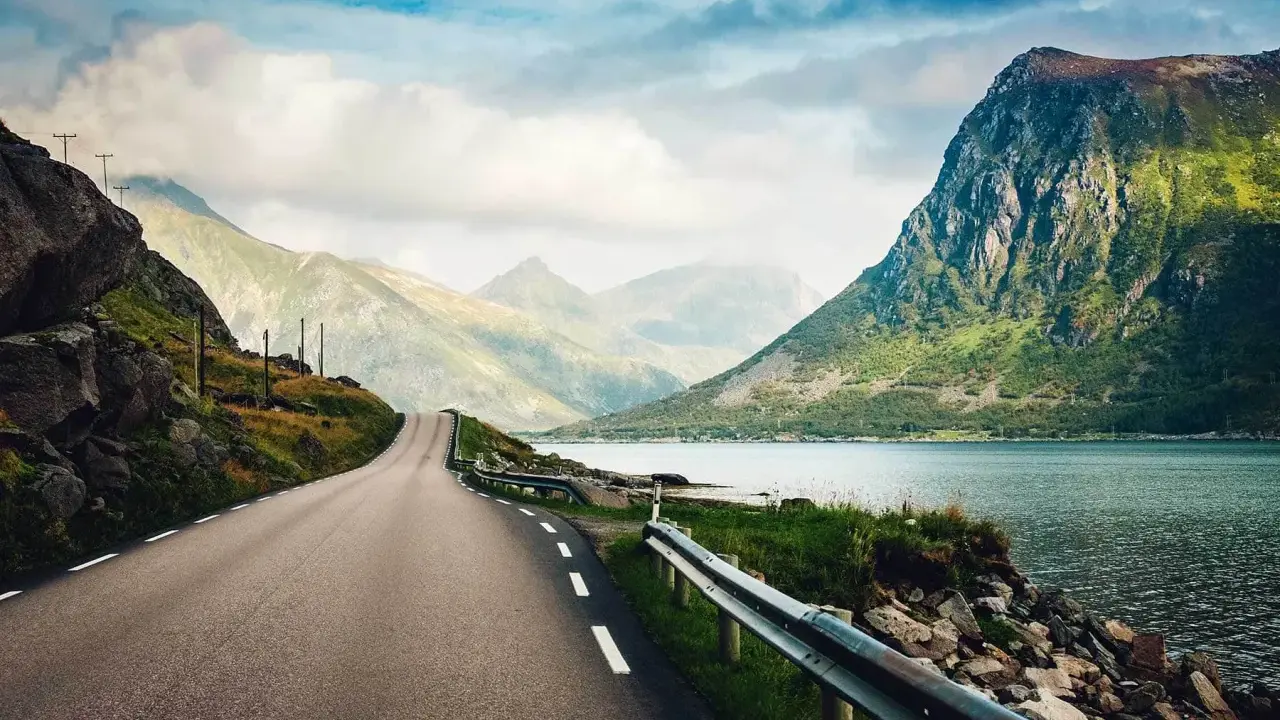 En slingrande väg leder mot dramatiska berg och en glittrande fjord. Drömmer om resor till Lofoten.